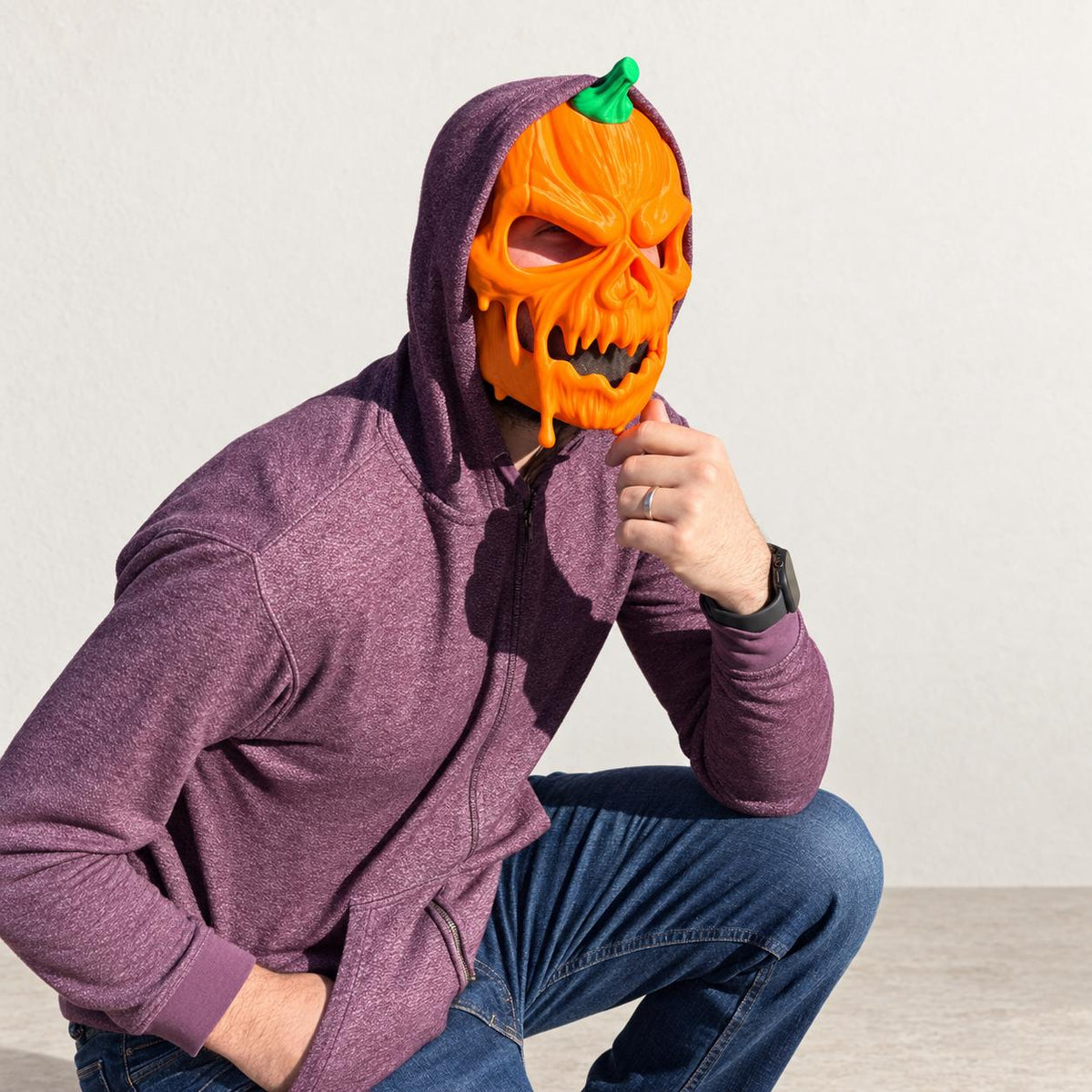 Person crouching while wearing the pumpkin skull mask and a hoodie